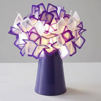 Simple Nordic style table lamp with metal base in assorted colours on a wooden table.