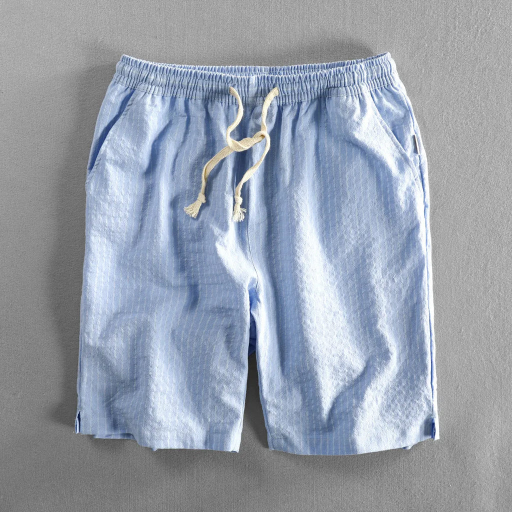 Man wearing loose straight-leg striped cotton shorts in a light colour, showing the mid waist and casual fit.