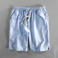 Man wearing loose straight-leg striped cotton shorts in a light colour, showing the mid waist and casual fit.