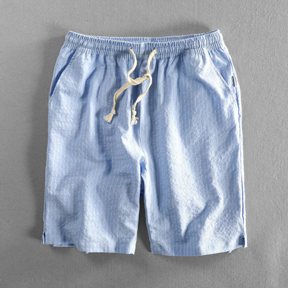 Man wearing loose straight-leg striped cotton shorts in a light colour, showing the mid waist and casual fit.