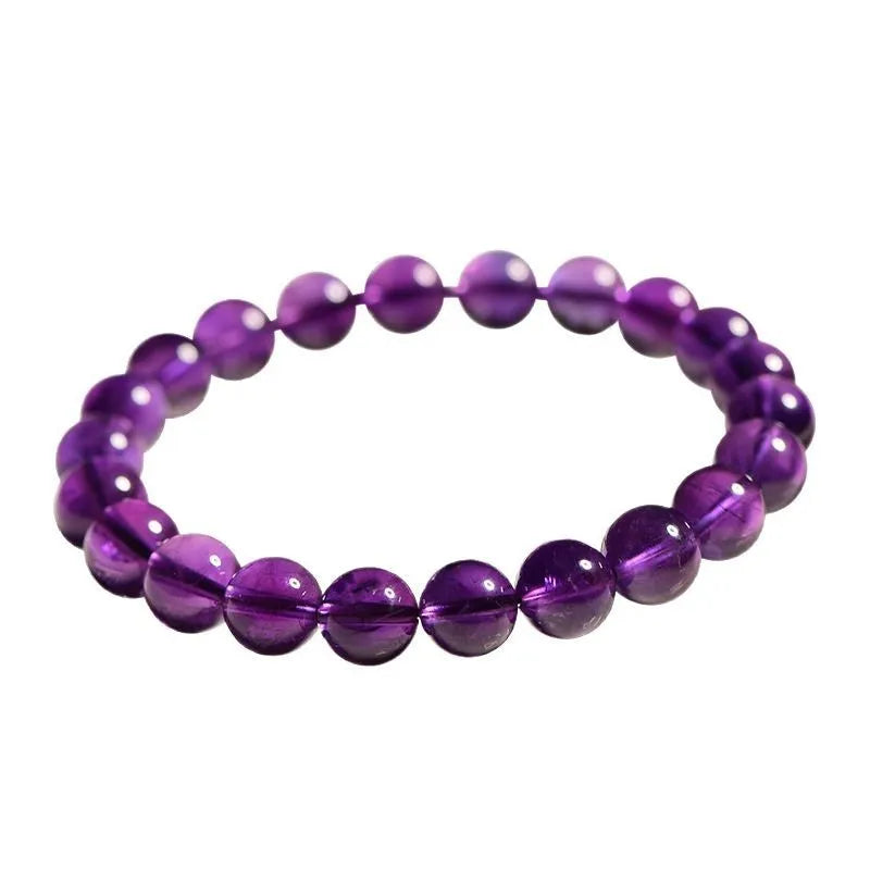 Natural violet amethyst crystal bead bracelet with polished, scattered beads on a neutral background.