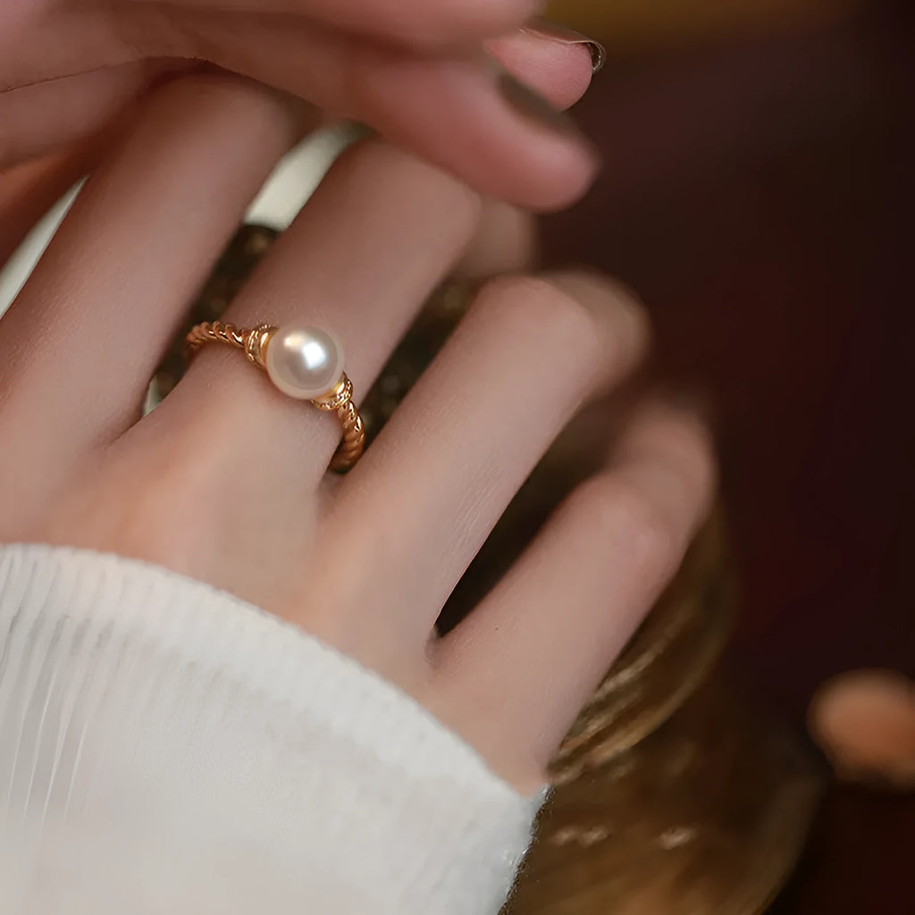 Adjustable geometric twist ring in copper with a central natural pearl on a model's finger.