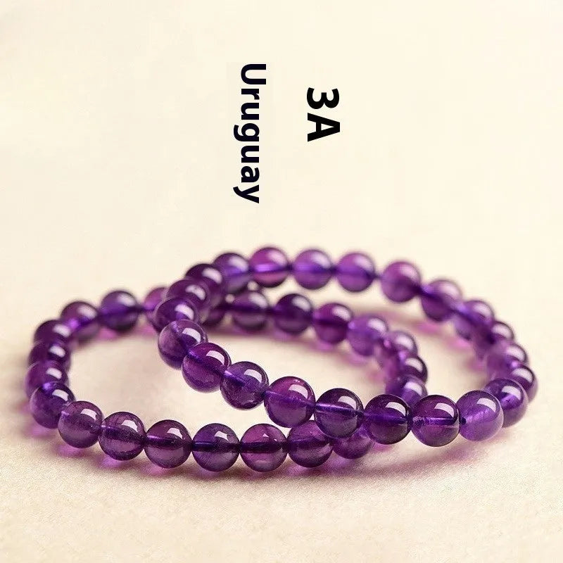 Natural violet amethyst crystal bead bracelet with polished, scattered beads on a neutral background.