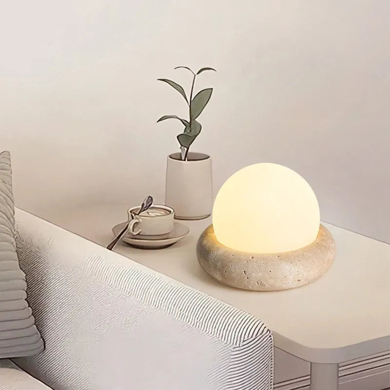 Cream coloured modern bedside night lamp with remote control on a table.