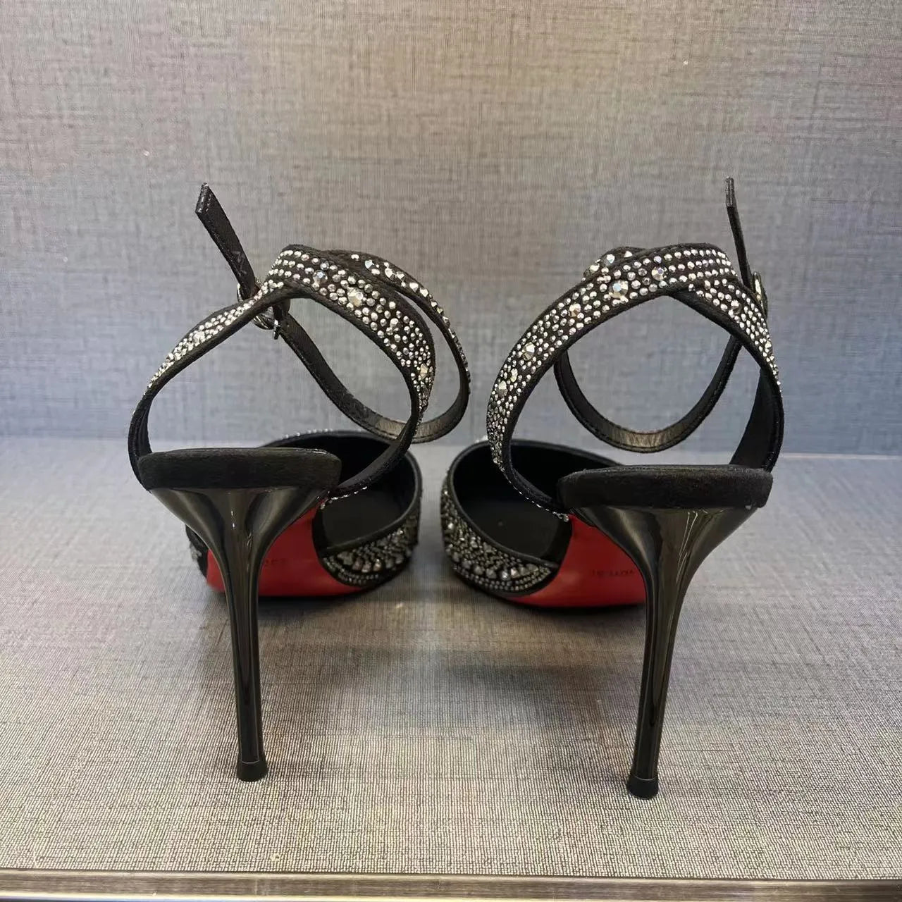 Women's black hollow high heel shoe with red sole, stiletto heel, and pointed toe on a plain background.