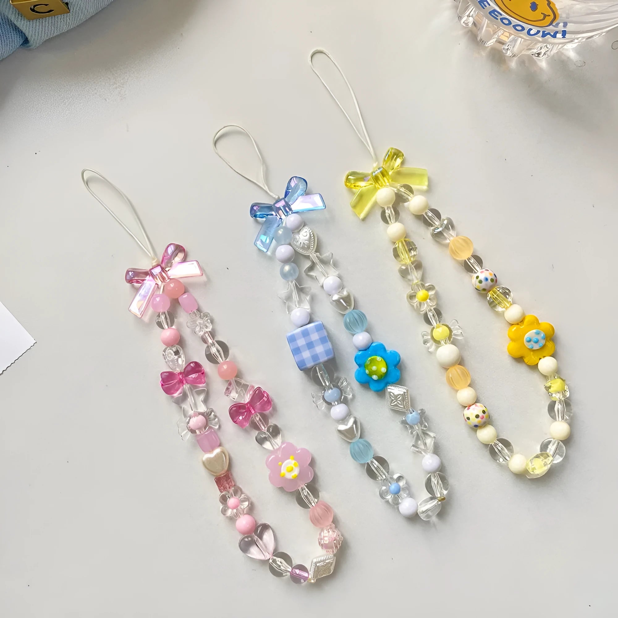 Adjustable rope wrist lanyard with blue plastic flower beads attached to a mobile phone.