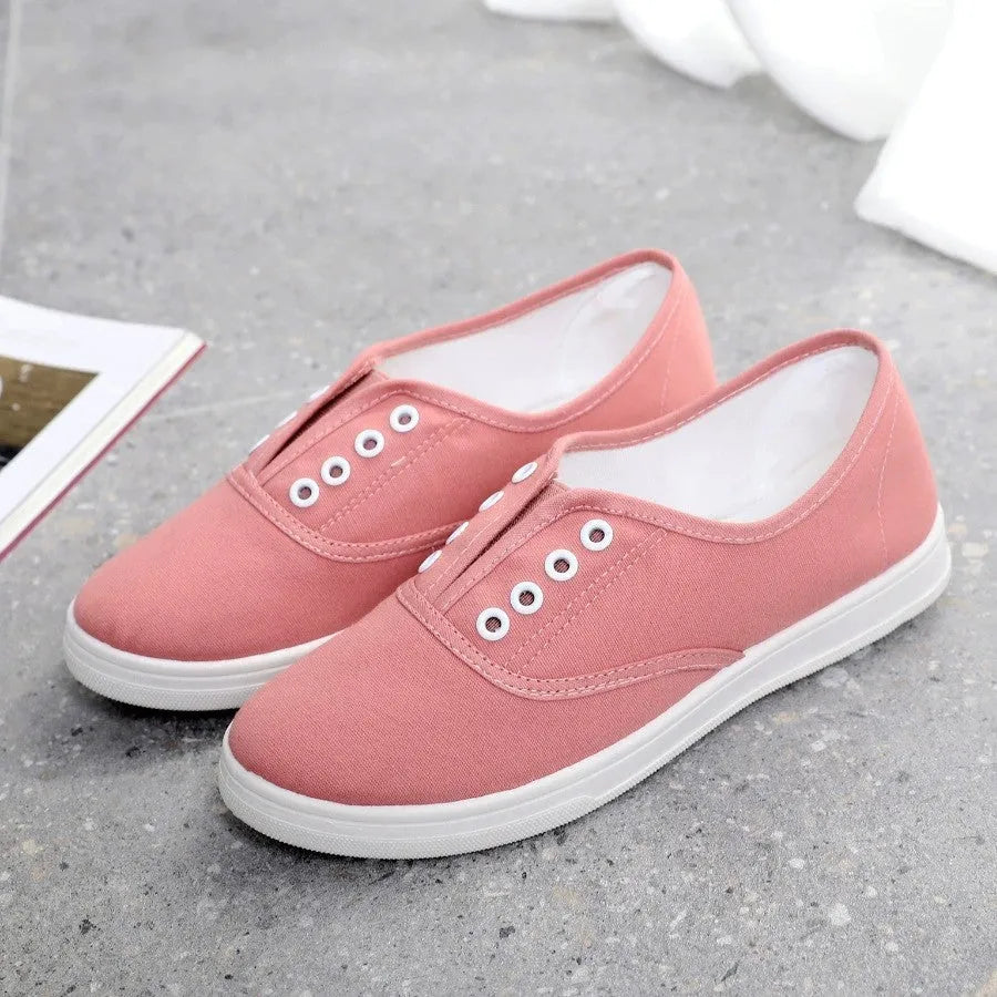 A pair of low-top casual canvas shoes in a flat style, shown in a choice of colours including black, white, grey, and pink.