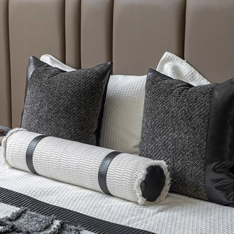 Grey and white plaid bed blanket draped over a dark grey duvet with a matching pillowcase and round leather-look cushion.