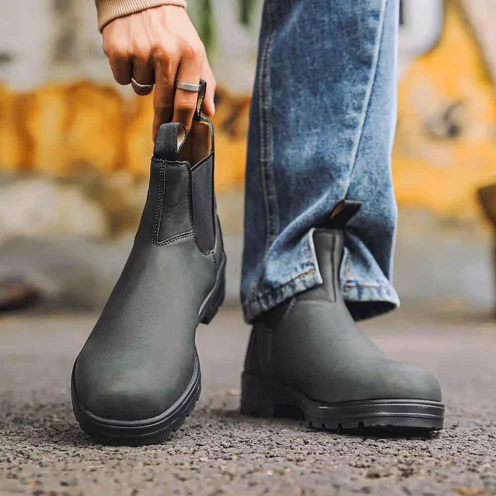 Vintage brown unisex Chelsea boot with round toe and beef tendon sole on a wooden floor.