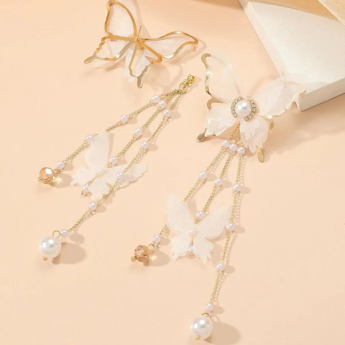 White butterfly-shaped earrings with pearls, rhinestones, and a tassel drop on a model's ear.