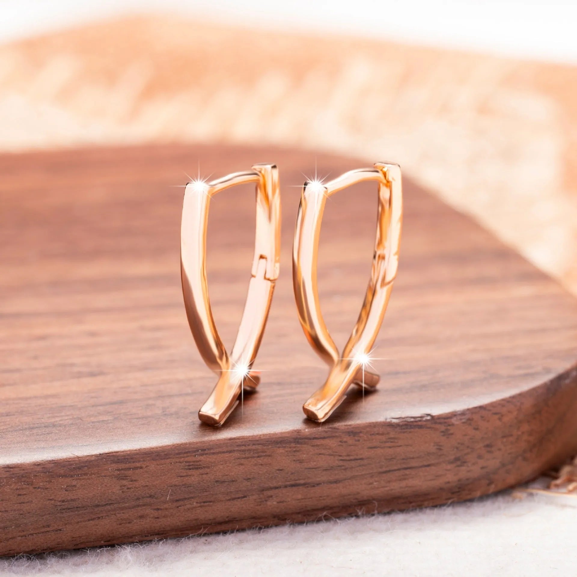 A pair of rose gold coloured cross-shaped earrings made from copper on a plain background.