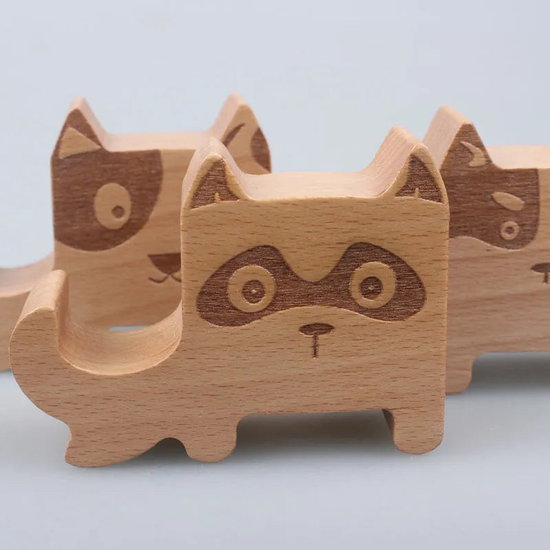 Solid beech wood mobile phone stand with a resin cow figurine and a slot for holding coins on a wooden desk.