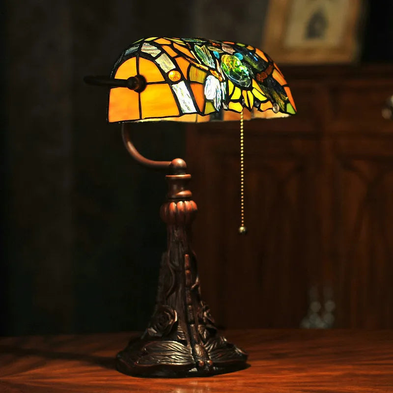 Tiffany style table lamp with coloured stained glass shade and resin base on a desk.