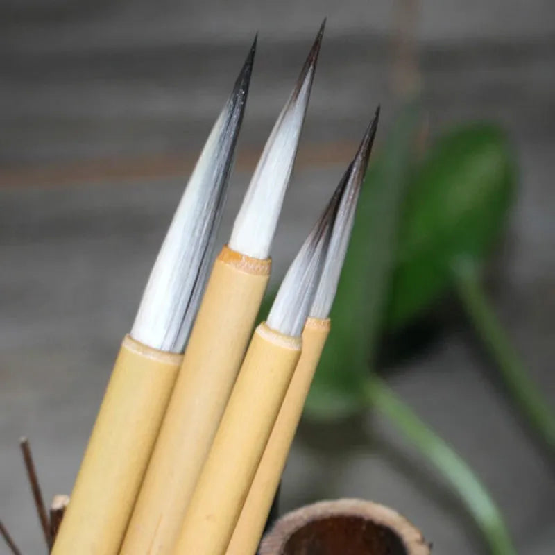 Four gold-coloured thin writing brushes with pine branch design, size 0, on a flat surface.