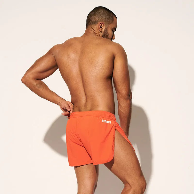 Man wearing loose orange red polyester beach shorts on sand