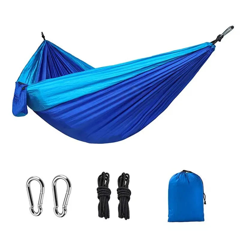 A sapphire blue parachute nylon hammock hung between two trees in a woodland setting.