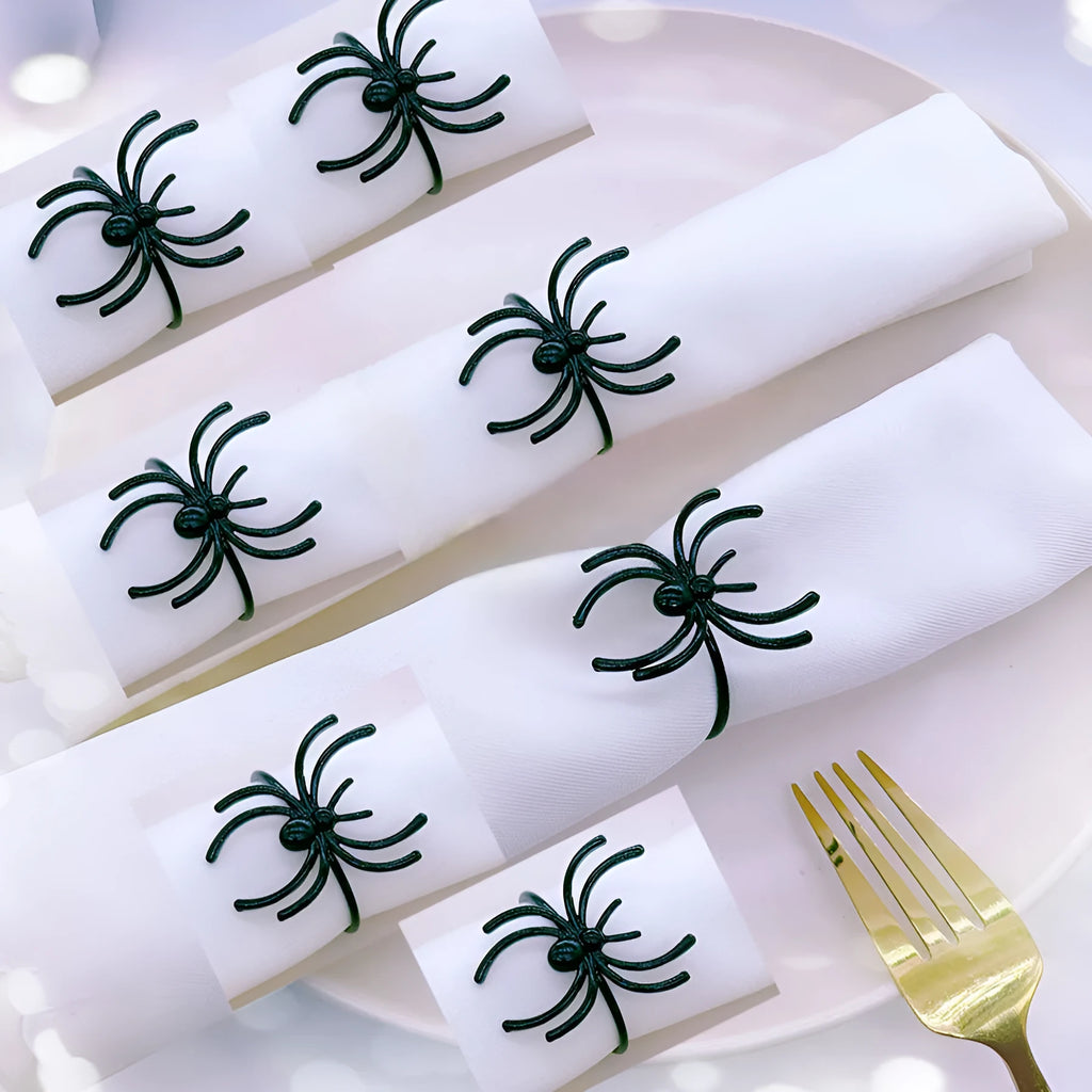 Six black alloy spider-shaped napkin rings for Halloween table decoration on a dark tablecloth.
