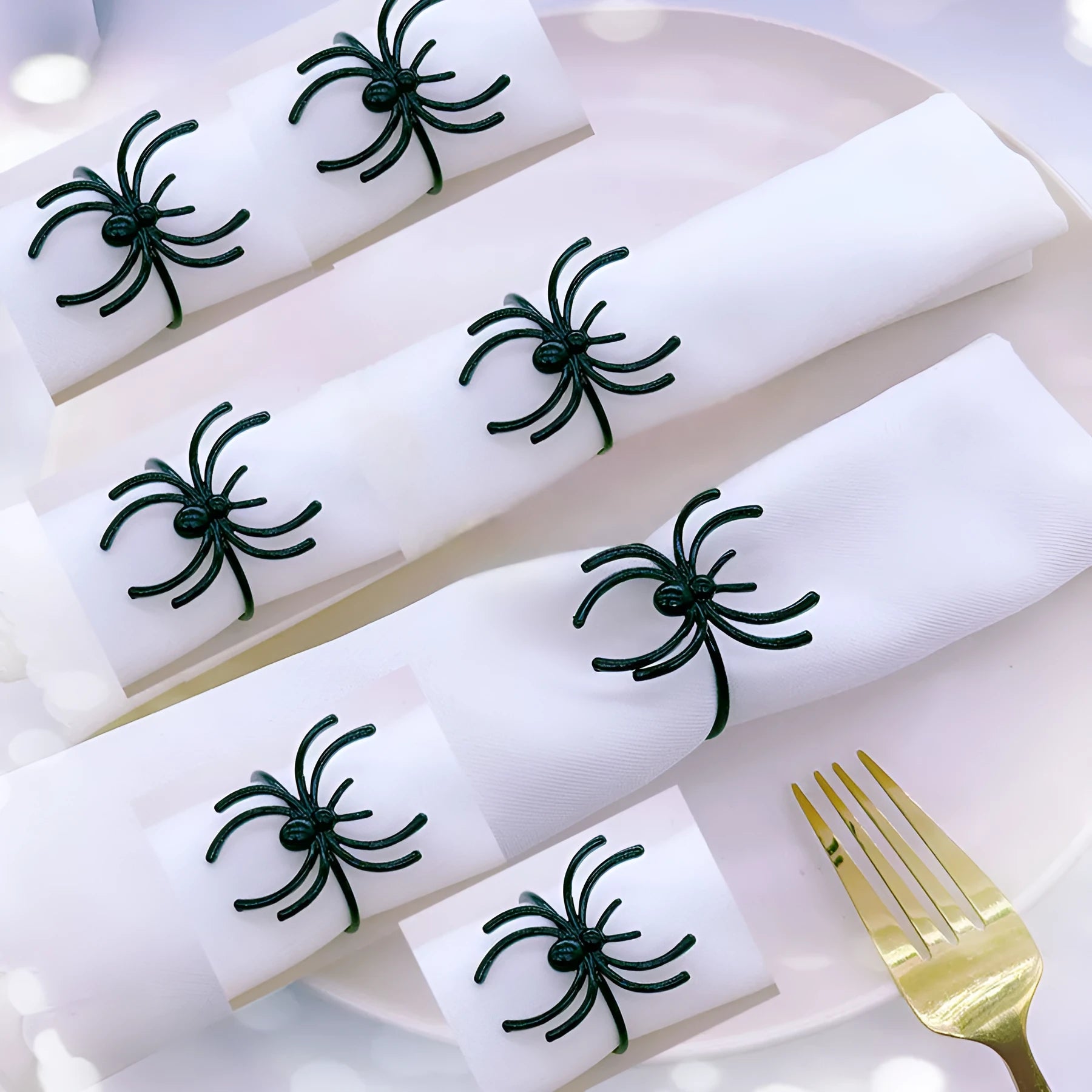 Six black alloy spider-shaped napkin rings for Halloween table decoration on a dark tablecloth.
