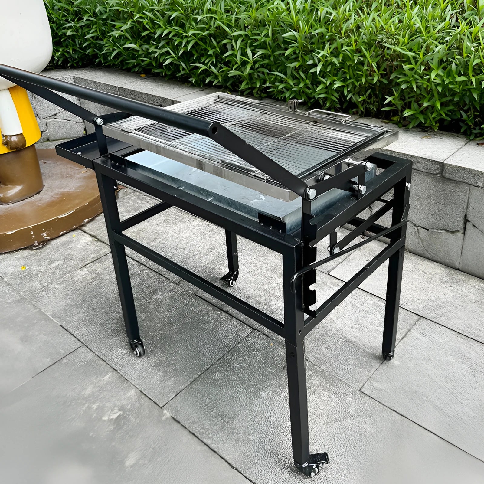 Foldable charcoal BBQ stove with a detachable grill, set up in an outdoor garden.
