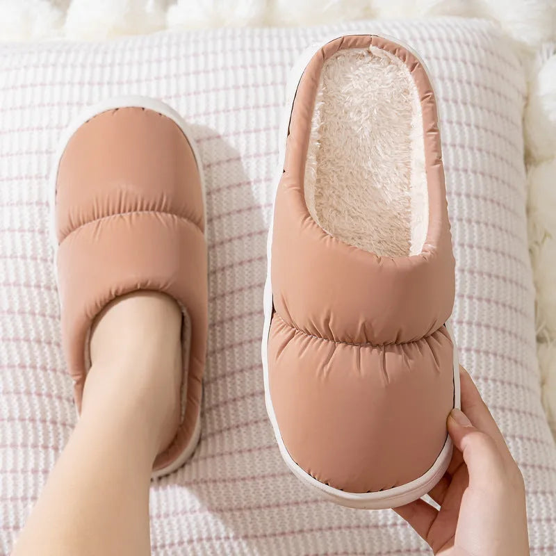A pair of blue down cotton winter slippers with a thick rubber sole and plush lining on a wooden floor.