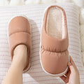 A pair of blue down cotton winter slippers with a thick rubber sole and plush lining on a wooden floor.