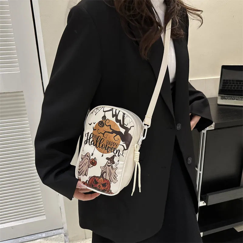 Black Halloween crossbody bag with orange pumpkin, white ghost, and bat graffiti print, shown worn across the body.