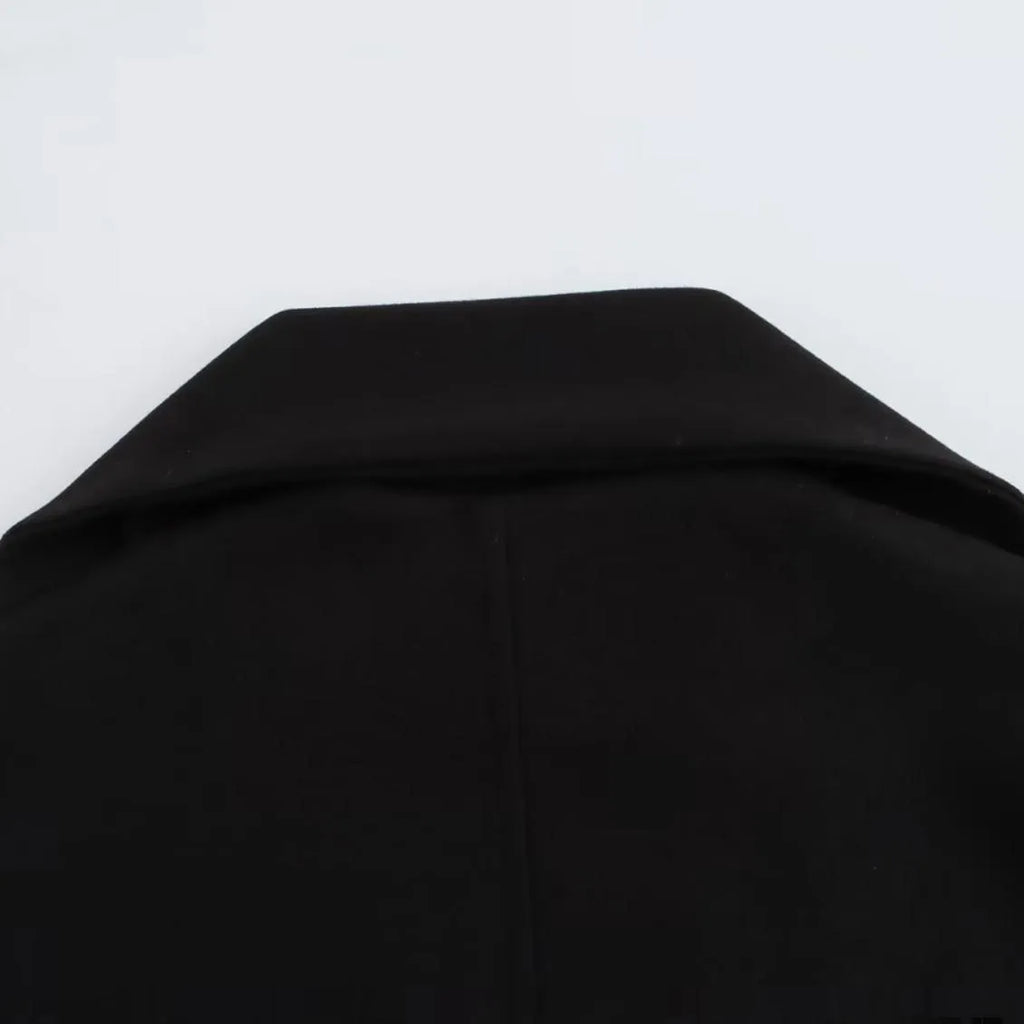 Women's long black coat with a grey artificial fur collar and side pockets, shown in a street fashion setting.