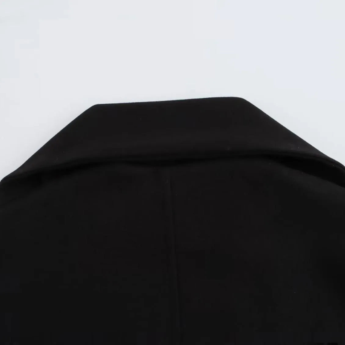 Women's long black coat with a grey artificial fur collar and side pockets, shown in a street fashion setting.