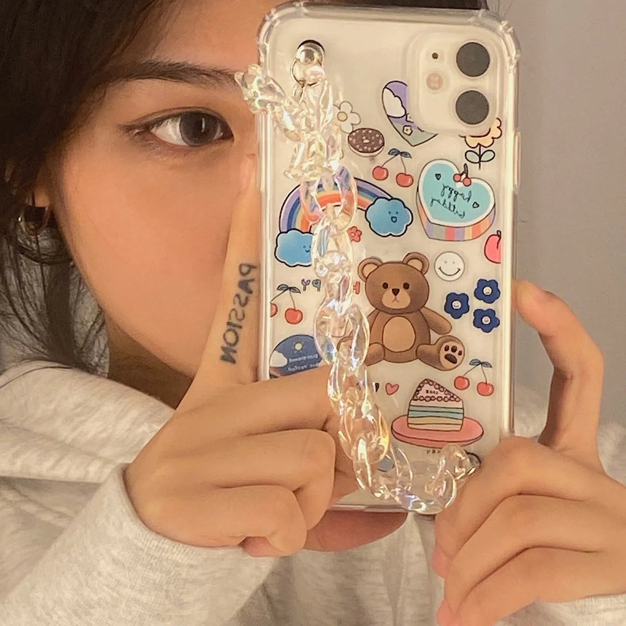 White iPhone case with a cartoon bear design and a connected silver bear pendant on a chain.