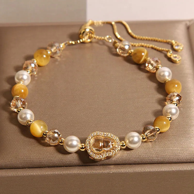 Yellow tiger's eye glass gourd pendant bracelet with alloy inlay and stone accents on a wrist.