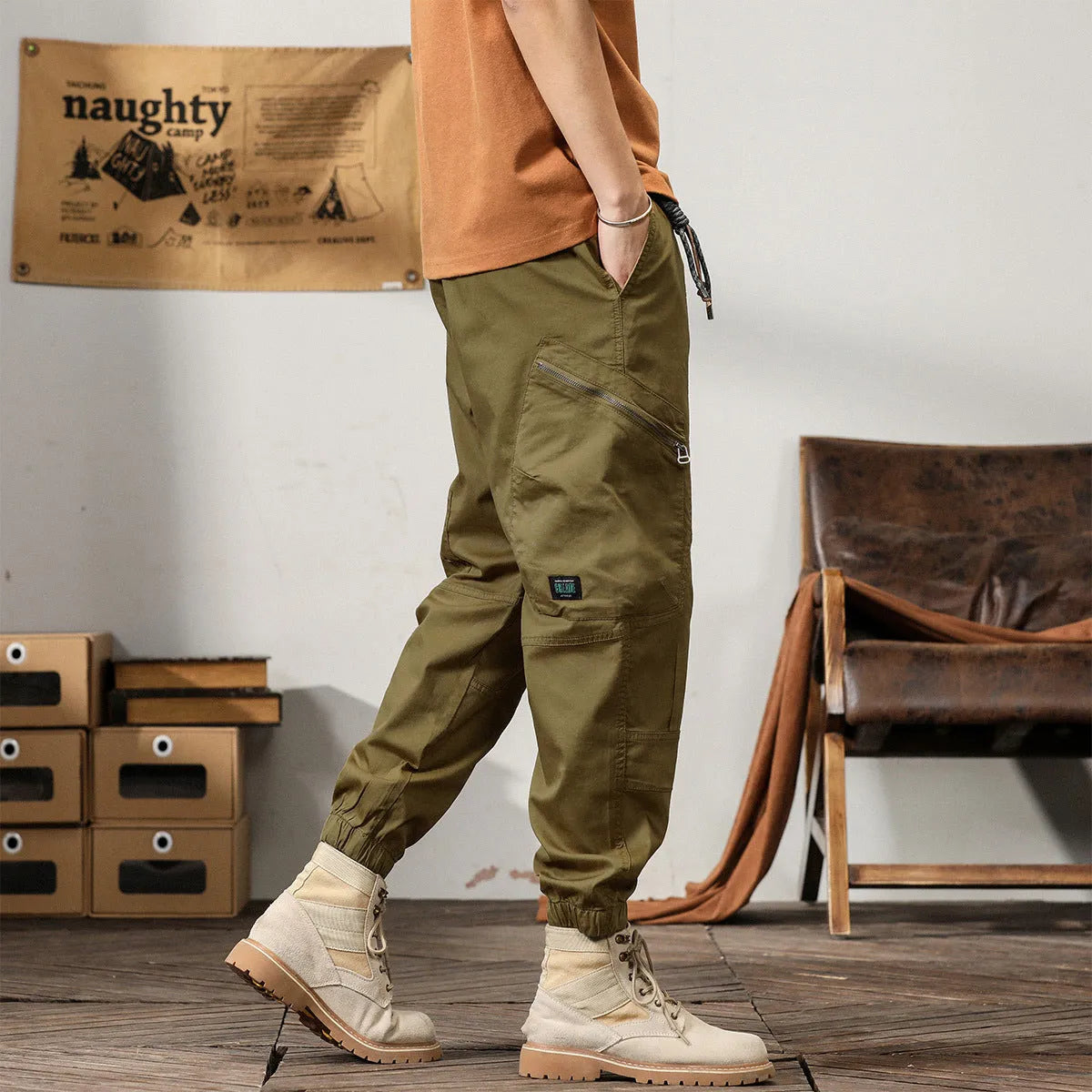 Man wearing khaki coloured cotton overalls with tapered legs and elasticated ankle bands.