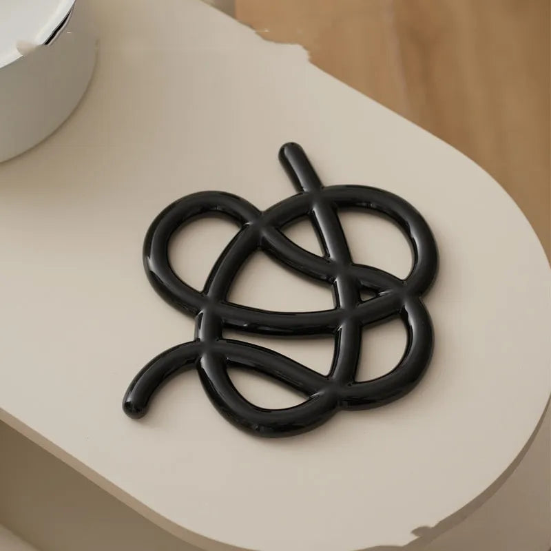 Modern irregular-shaped ceramic heat proof mat in grey protecting a wooden dining table from a hot pan.