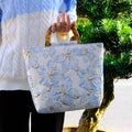 Light blue canvas shoulder bag with bronzing flower pattern, showing square shape and double shoulder straps