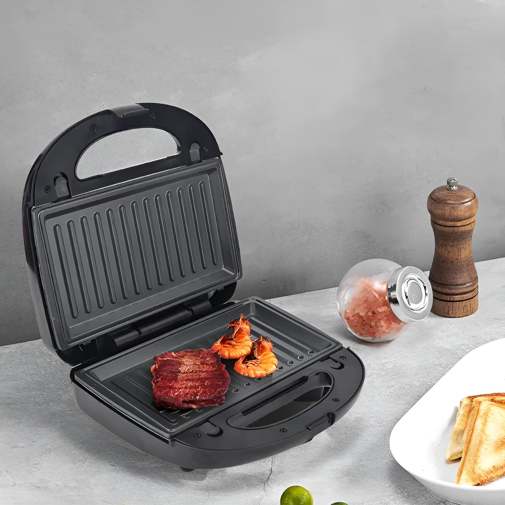 Black electric sandwich pan with brushed stainless steel lid and six non-stick cooking plates on a kitchen counter.