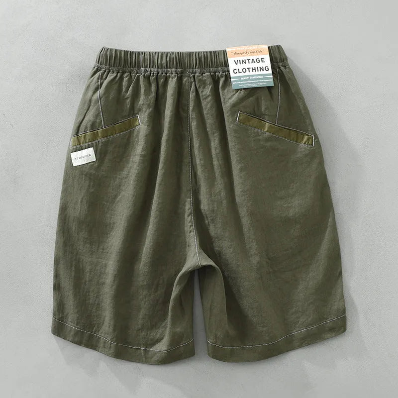 Man wearing loose straight-leg linen shorts in green, showcasing mid-waist and drawstring detail.