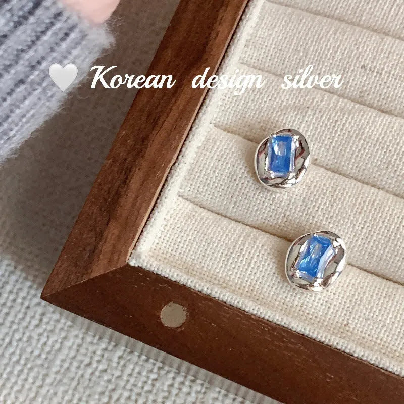 Women's sterling silver earrings with oval heart-wrapped design and blue diamond accents