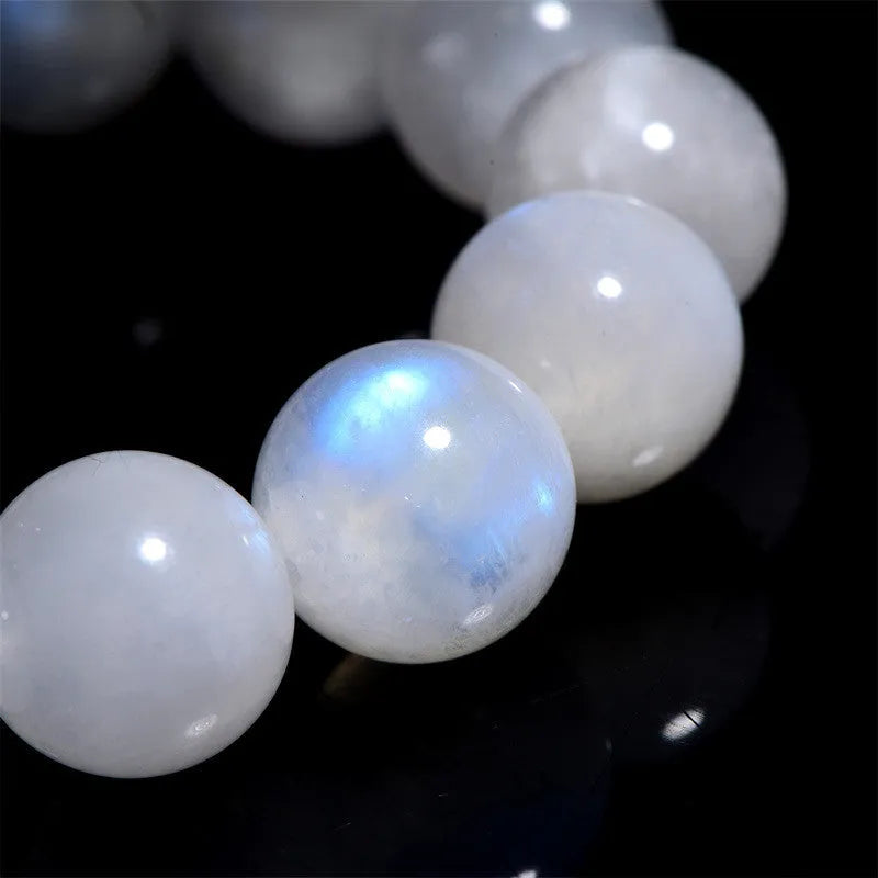 Natural white moonstone bracelet with round polished beads showing a blue sheen, laid flat.