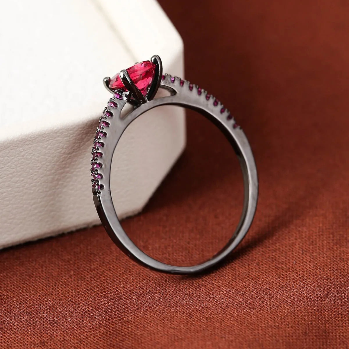 A hexagonal geometric ring with a zircon stone, shown in a gun black and rose red electroplated finish on a finger.