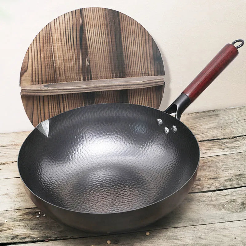 Black handmade traditional iron wok with a long wooden handle, shown with a glass lid.