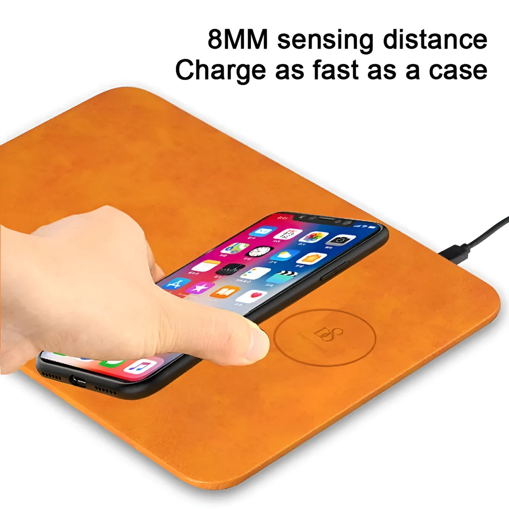Brown leather wireless charging mouse pad on a wooden desk with a phone charging on it.