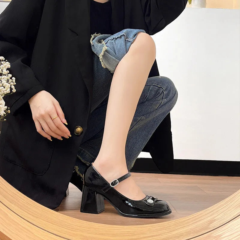 Women's black patent leather wide fit court shoes with a round toe and chunky buckle fastening heel.