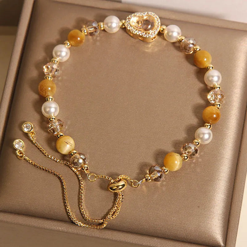 Yellow tiger's eye glass gourd pendant bracelet with alloy inlay and stone accents on a wrist.
