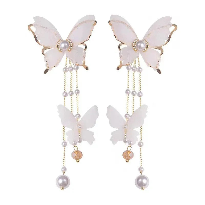 White butterfly-shaped earrings with pearls, rhinestones, and a tassel drop on a model's ear.