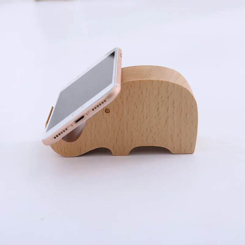 Solid beech wood mobile phone stand with a resin cow figurine and a slot for holding coins on a wooden desk.