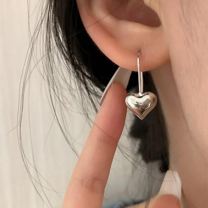 Silver glossy 3D heart-shaped earrings with Korean style hooks on a white background.