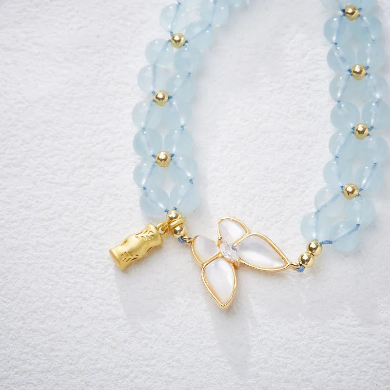 Close-up of a women's woven bracelet with 6mm aquamarine beads and a butterfly charm on a wrist.