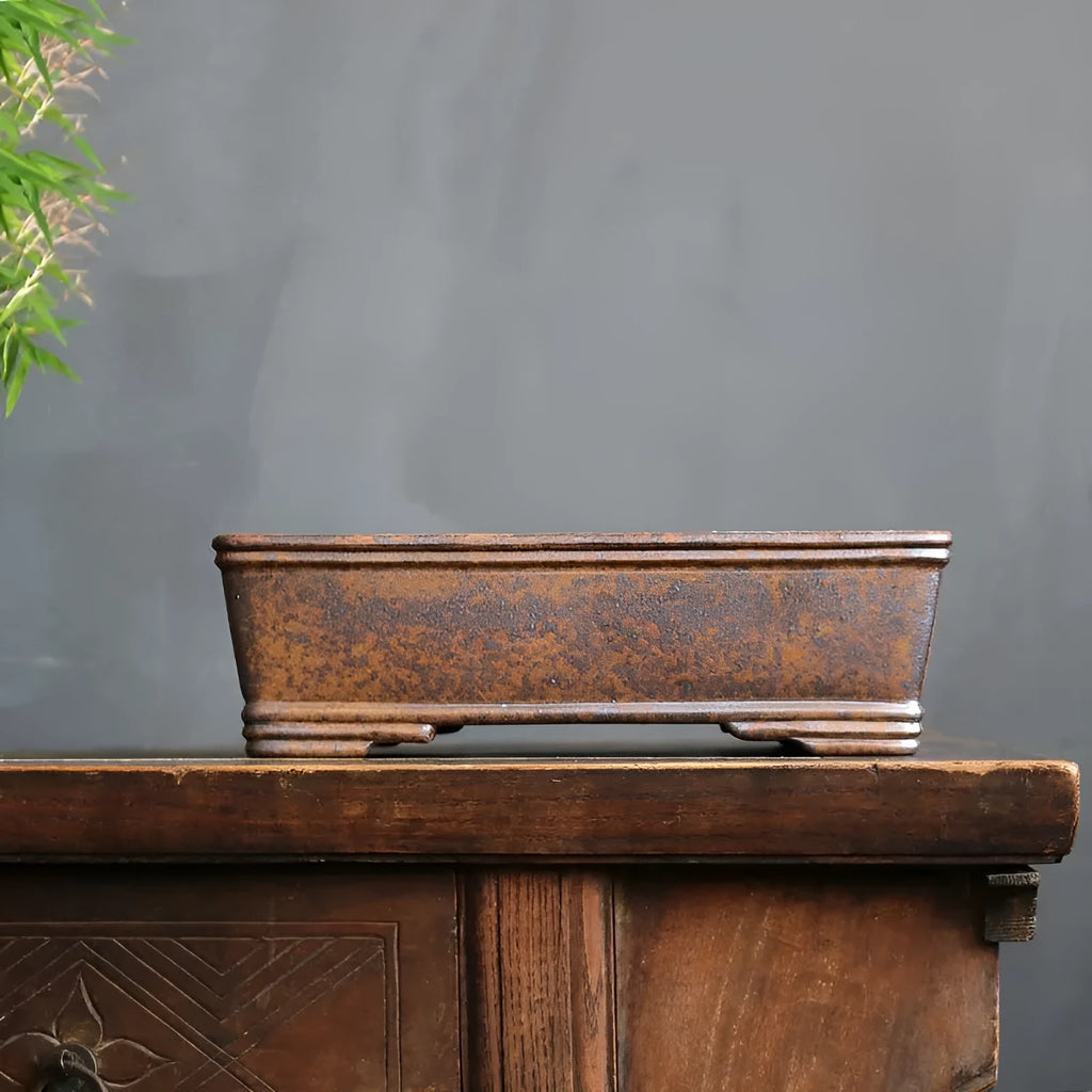 Rectangular purple sand bonsai pot with burnt pine tree decoration, shown on a garden surface.