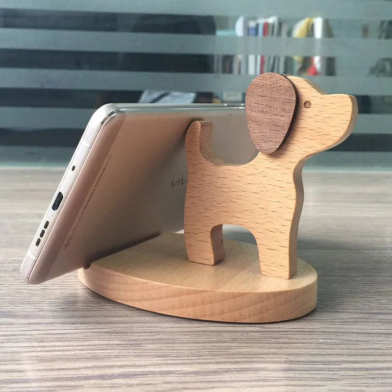 Solid beech wood mobile phone stand with a resin cow figurine and a slot for holding coins on a wooden desk.