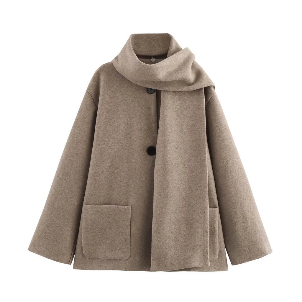 Women's long black coat with a grey artificial fur collar and side pockets, shown in a street fashion setting.