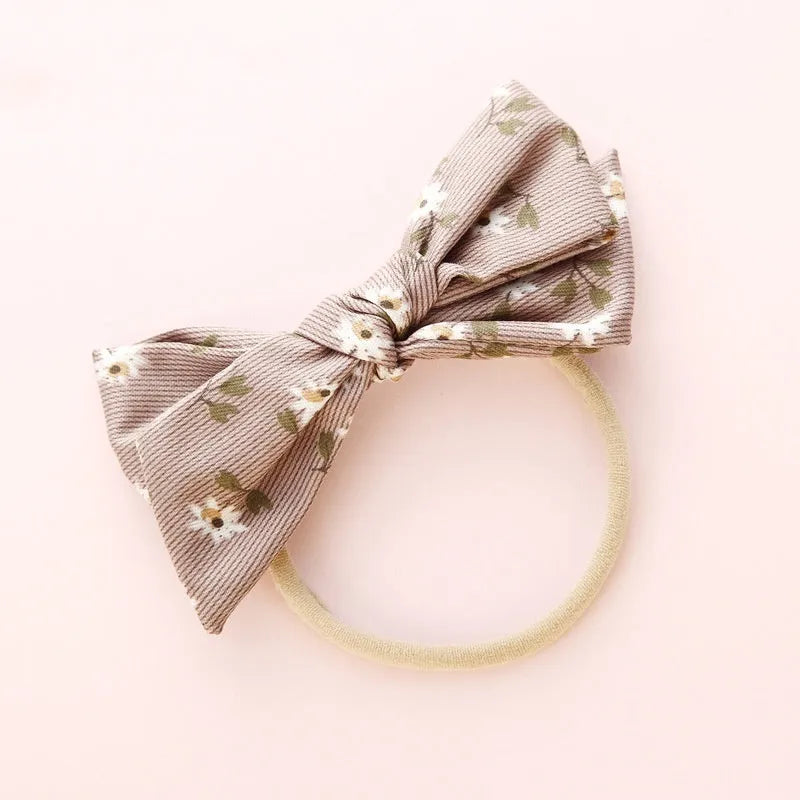 Children's cloth hair band with a white knotted bow, shown against a colour swatch background.